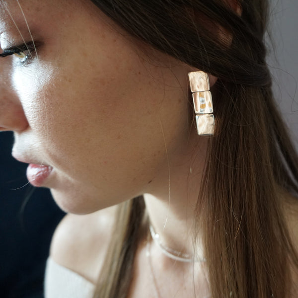 brunette looking down side face closeup wearing gold brass three square post earrings