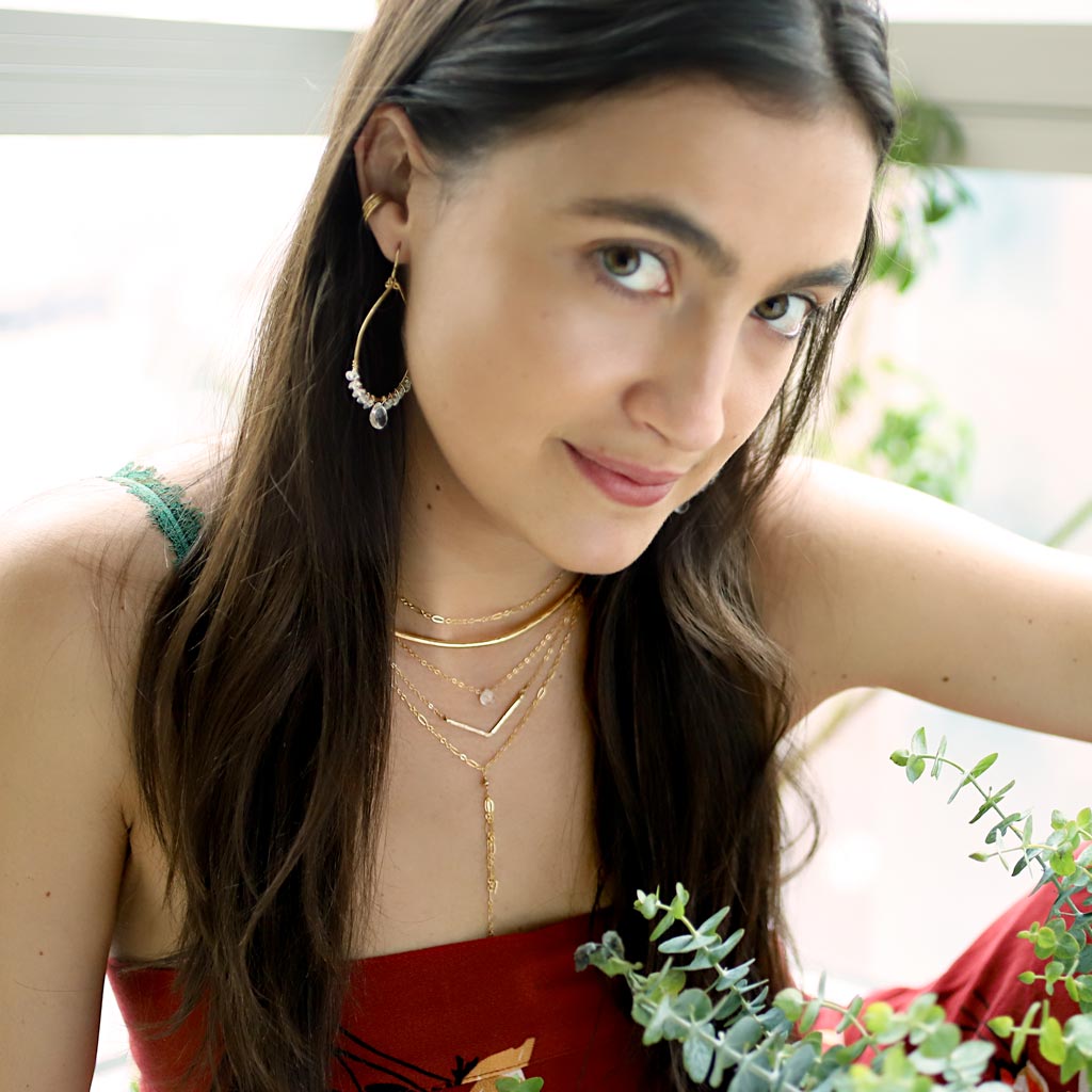 red blouse brunette looking at camera wearing 14k gold filled crystal quartz and aquamarine teardrop gemstone arc earrings
