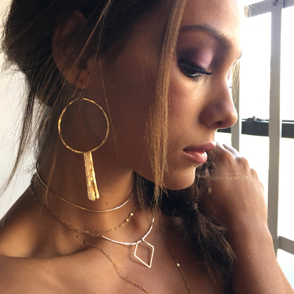brunette looking down wearing 14k gold filled xl round fringe hoops