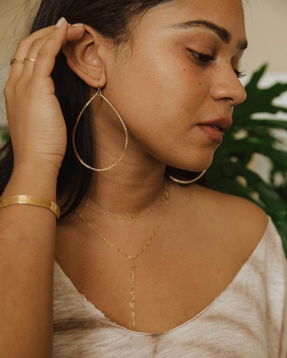 brunette on a white tshirt looking down wearing 14k gold filled xl teardrop hoop earrings