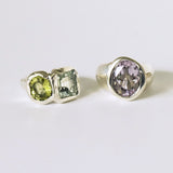 Two silver rings with gemstones including lemon citrine green amethyst and pink amethyst on a light gray background