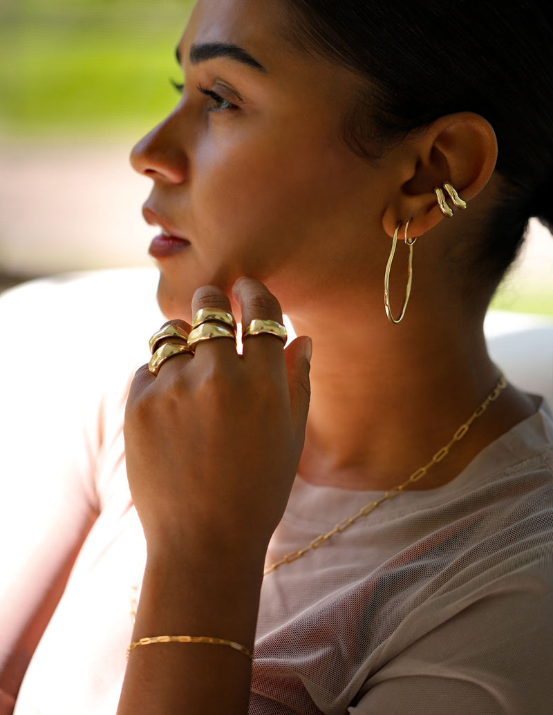 girl with multiple stacked gold rings, hoop earrings and cartilage hug hoops