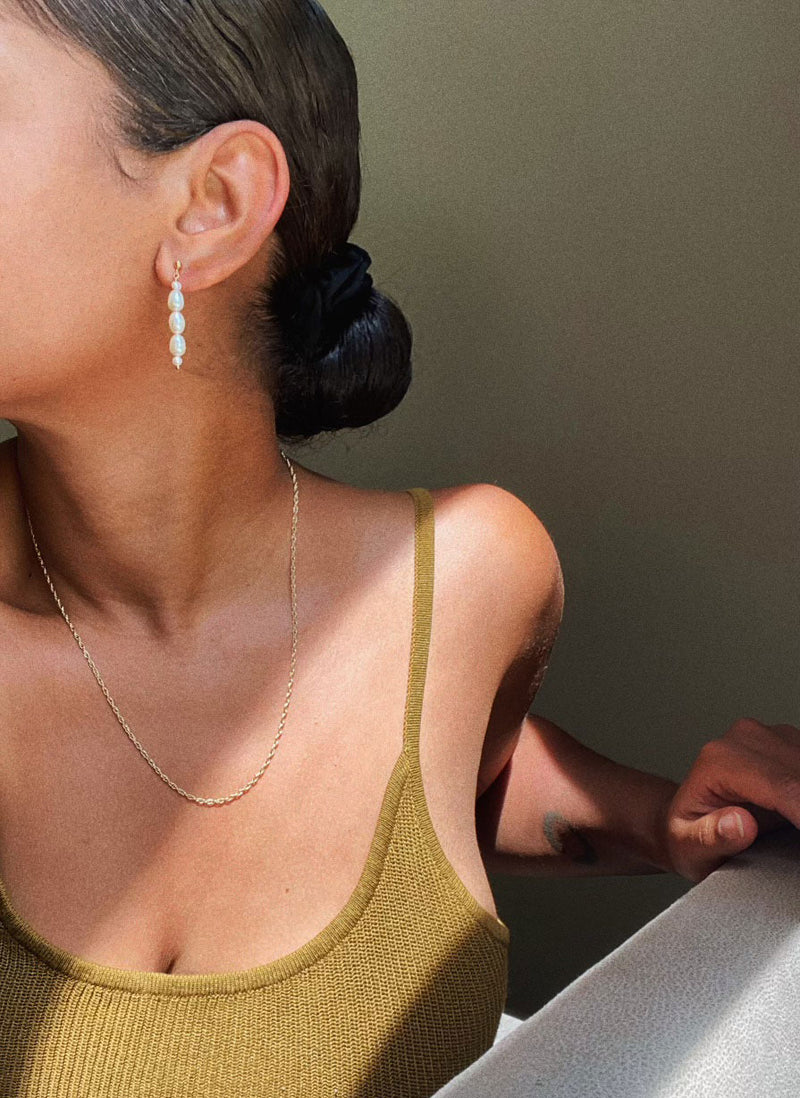 profile of woman with pearl drop earrings and simple chain necklace wearing a green dress