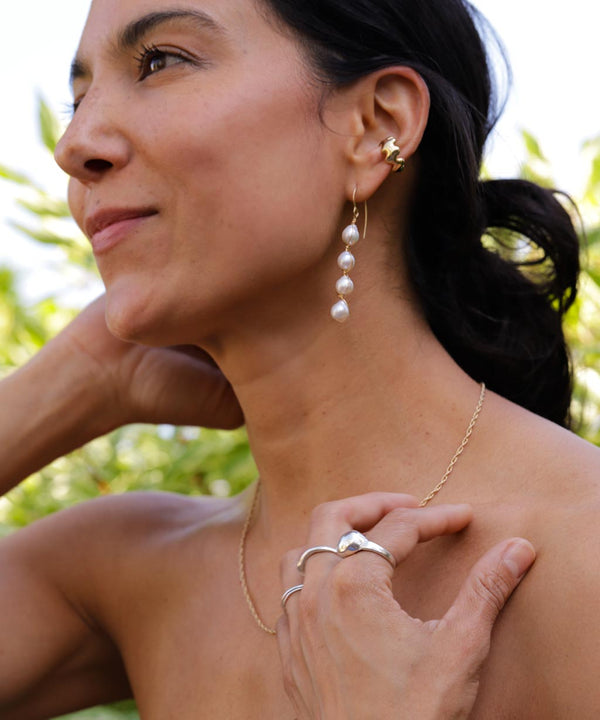 girl wearing 4 pearl drop earrings and a wavy gold cartilage hoop wearing silver rings