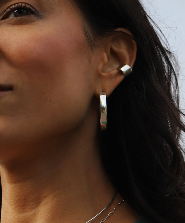 woman's ear with wide silver hoop earrings 