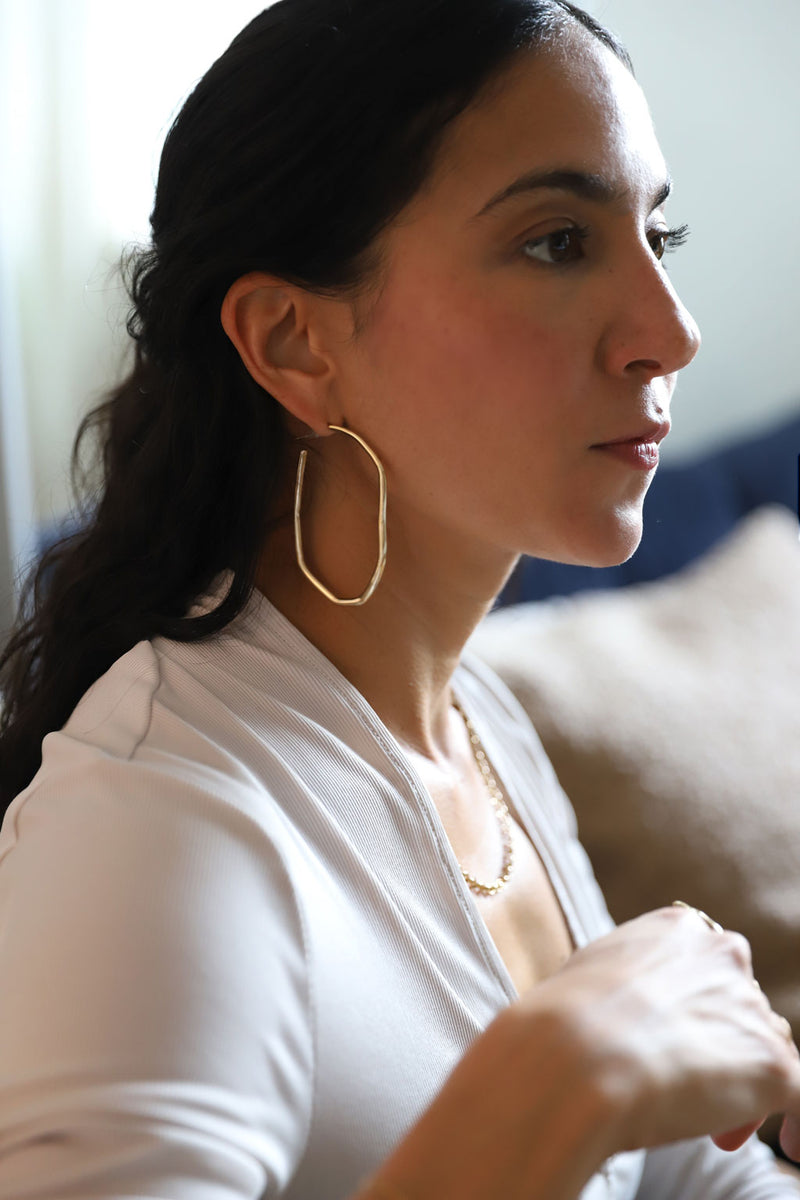 profile of a woman with black hair and large gold irregular hoops