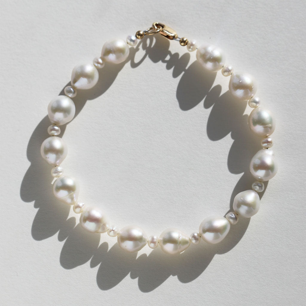 alternating large and small white freshwater pearl bracelet with gold clasp on white background