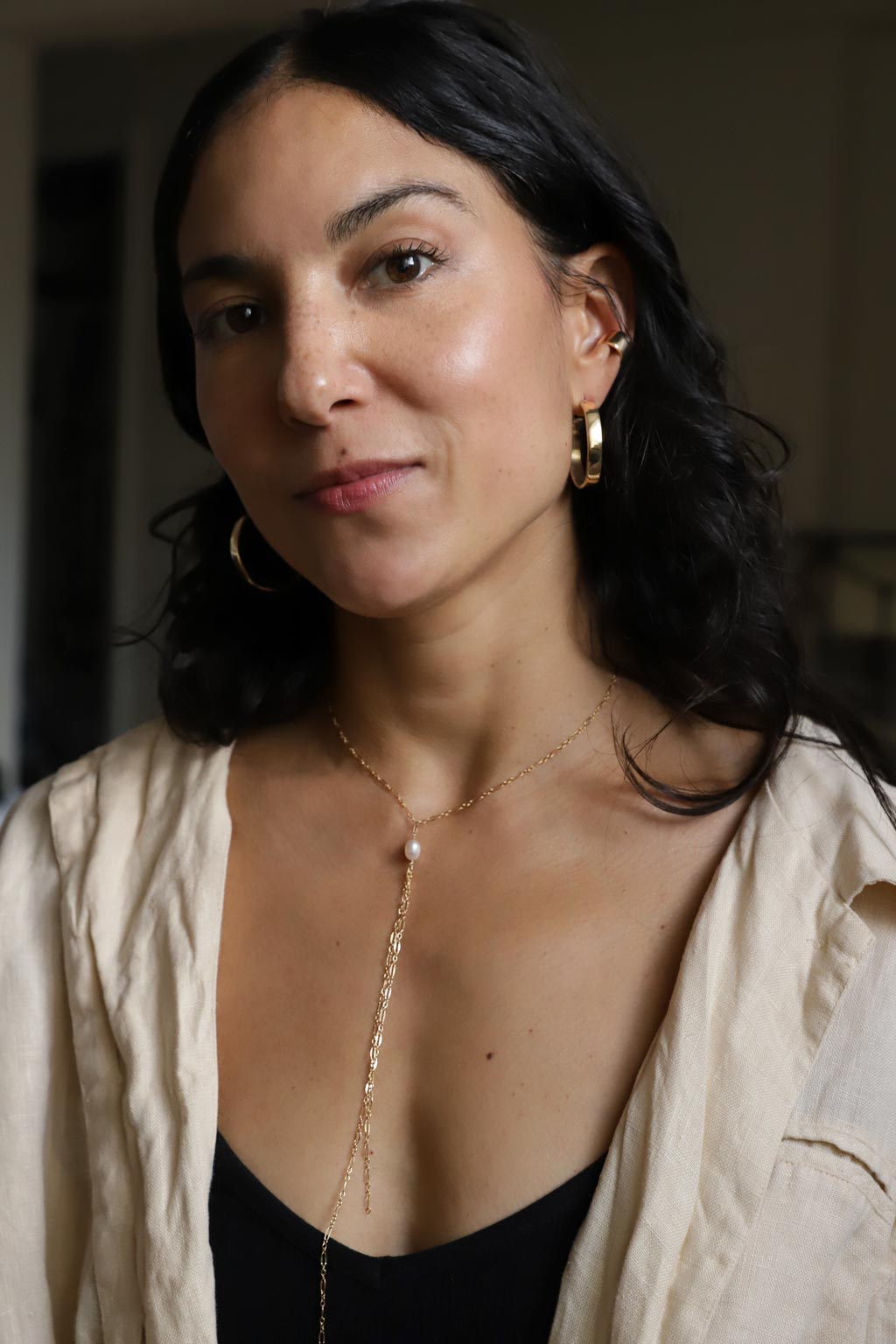 girl with gold hoop earrings and a delicate gold pearl y shaped necklace against a dark background