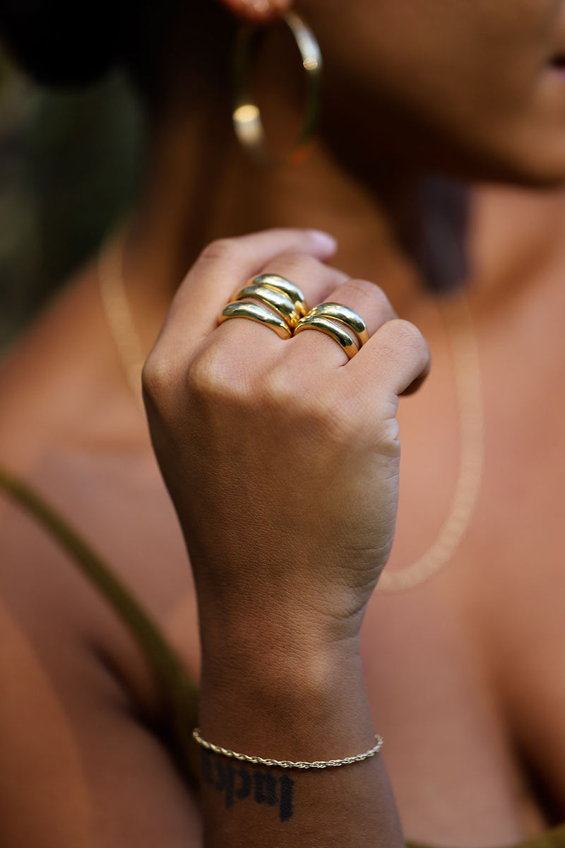 hand with muliple chunky gold bands and rope chain bracelet