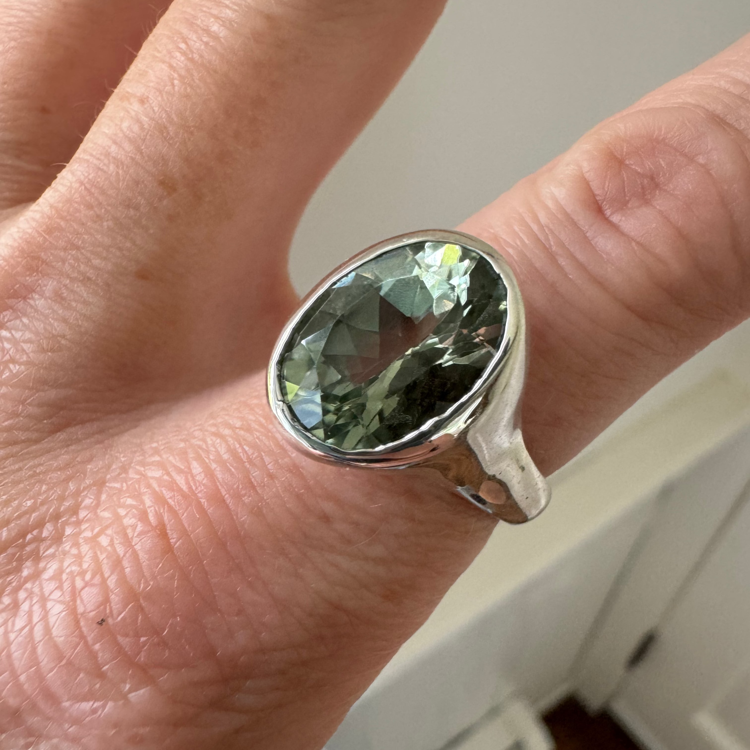 Silver ring with a green amethyst gemstone on a person's finger