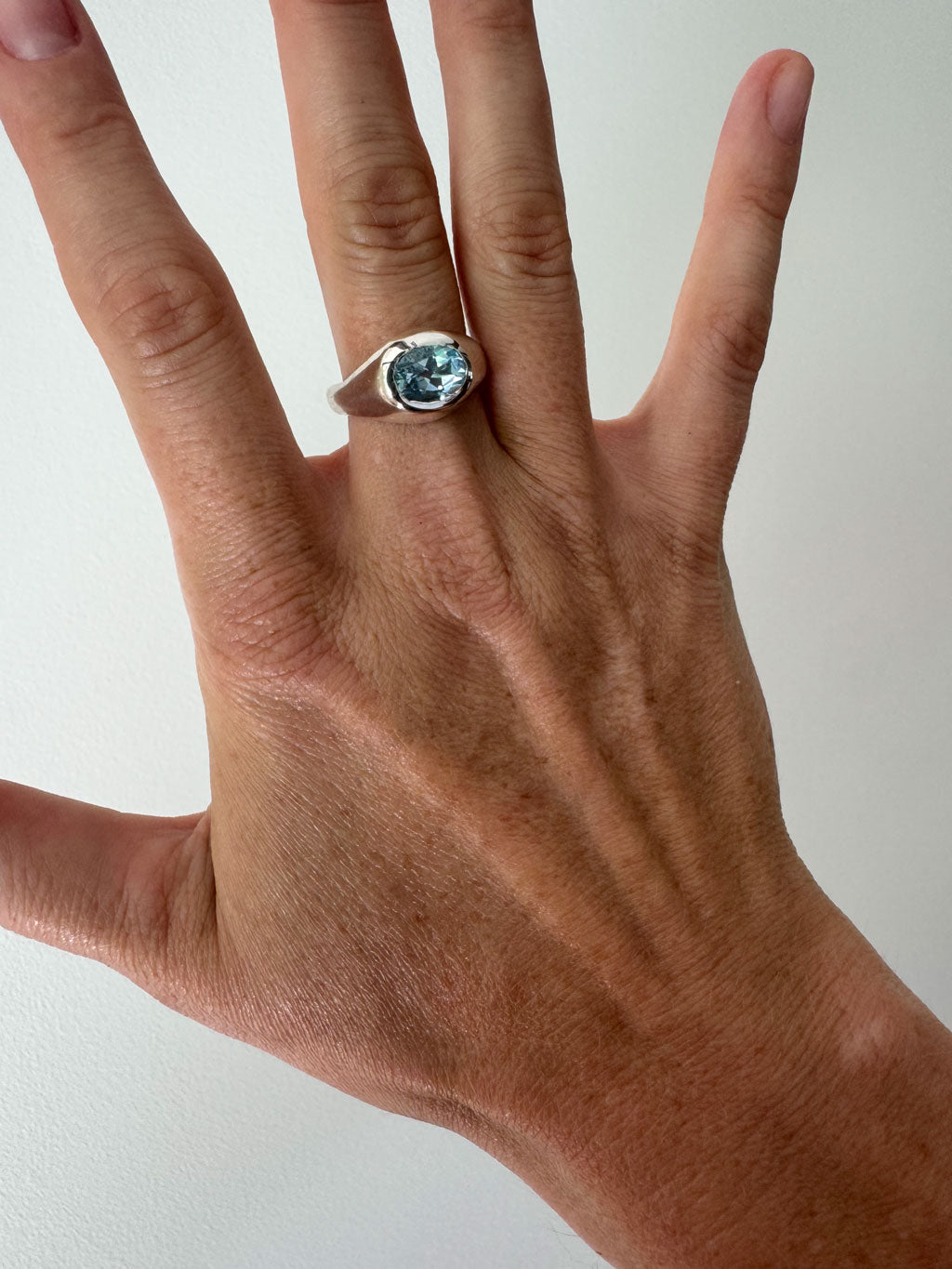 Hand wearing a ring with a blue gemstone on a plain background