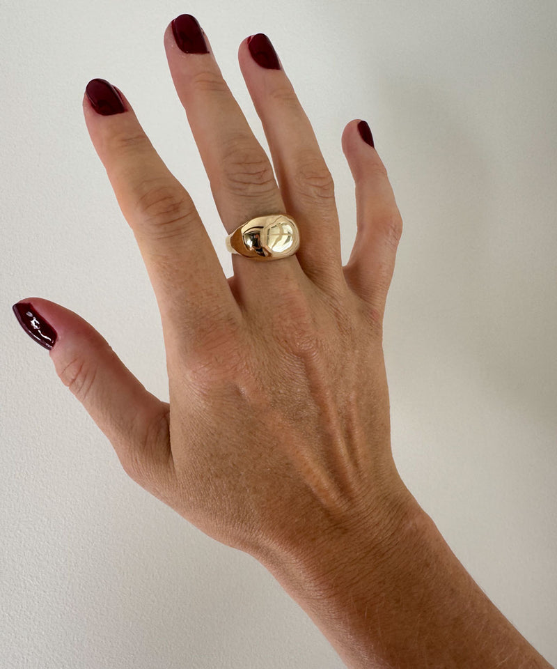 Hand wearing a gold ring with a plain background