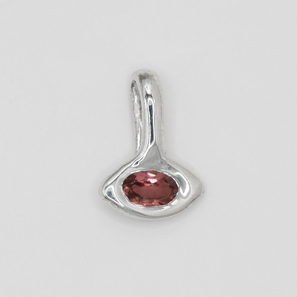 A sterling silver pendant with a unique organic, abstract shape featuring a central oval-cut pinkish-red gemstone, shown on a neutral light gray background.