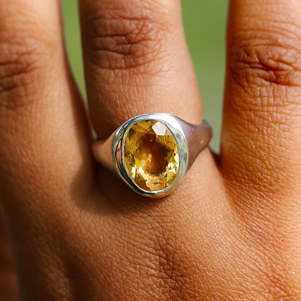 Close-up of a hand wearing a silver ring with a yellow gemstone.