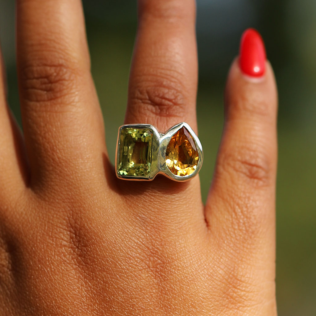 Ring with two gemstones on a person's finger against a blurred natural background