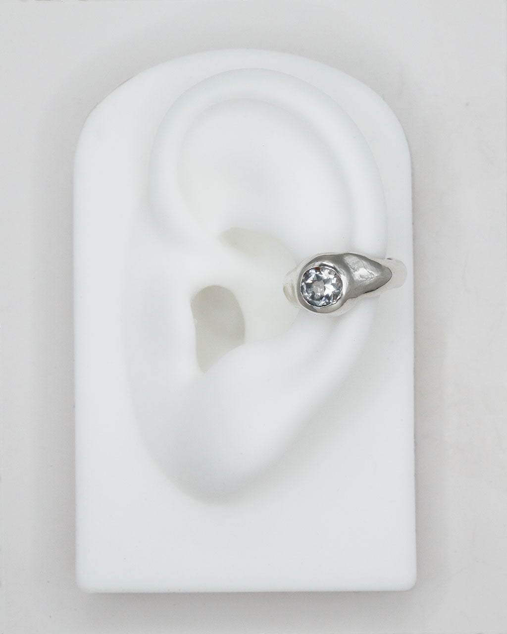 Silver earring with a clear gemstone on a white ear model