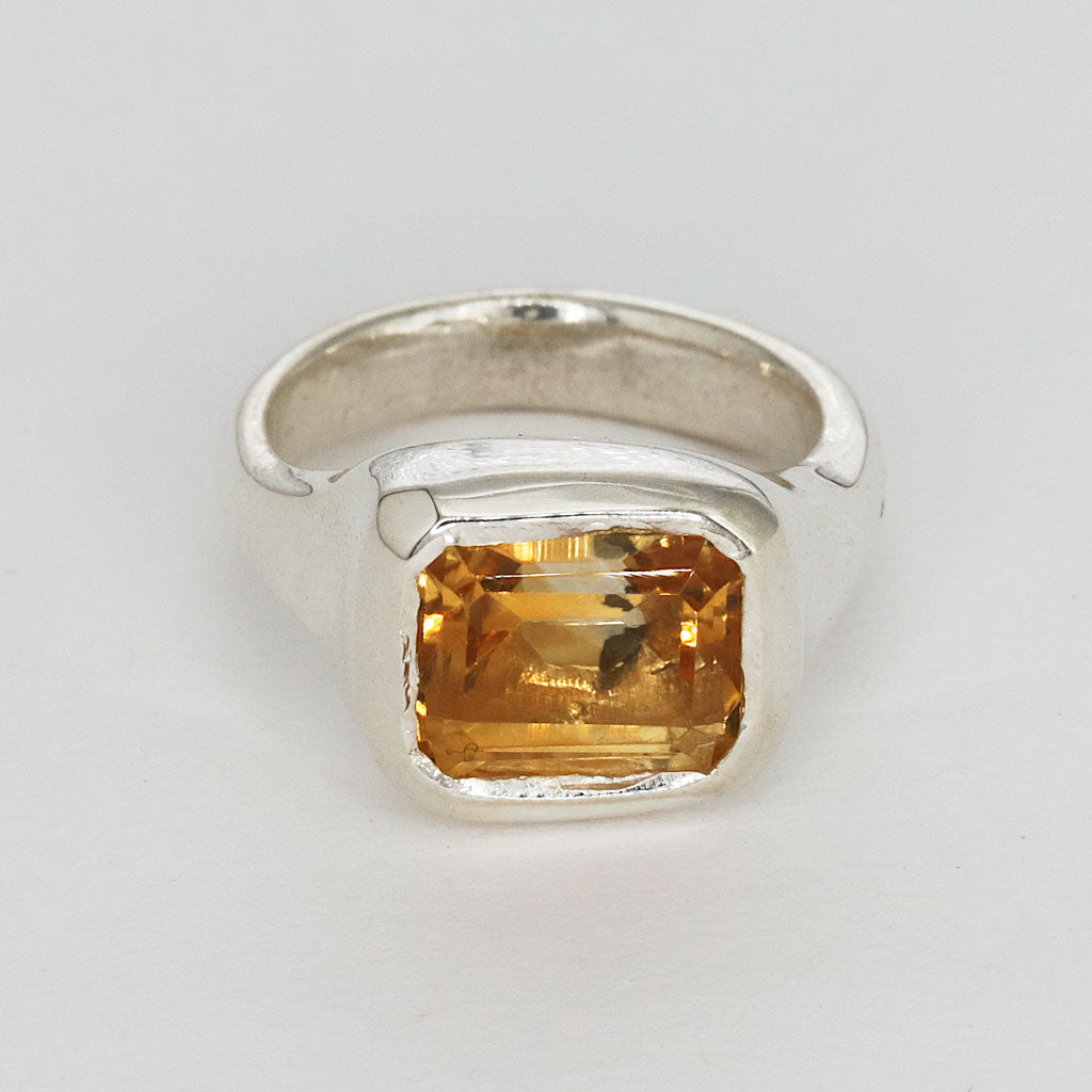 Silver ring with a yellow gemstone on a light gray background