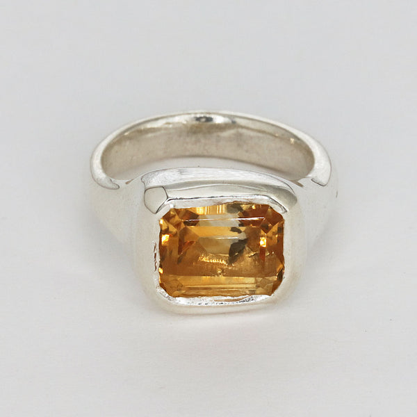 Silver ring with a yellow gemstone on a light gray background