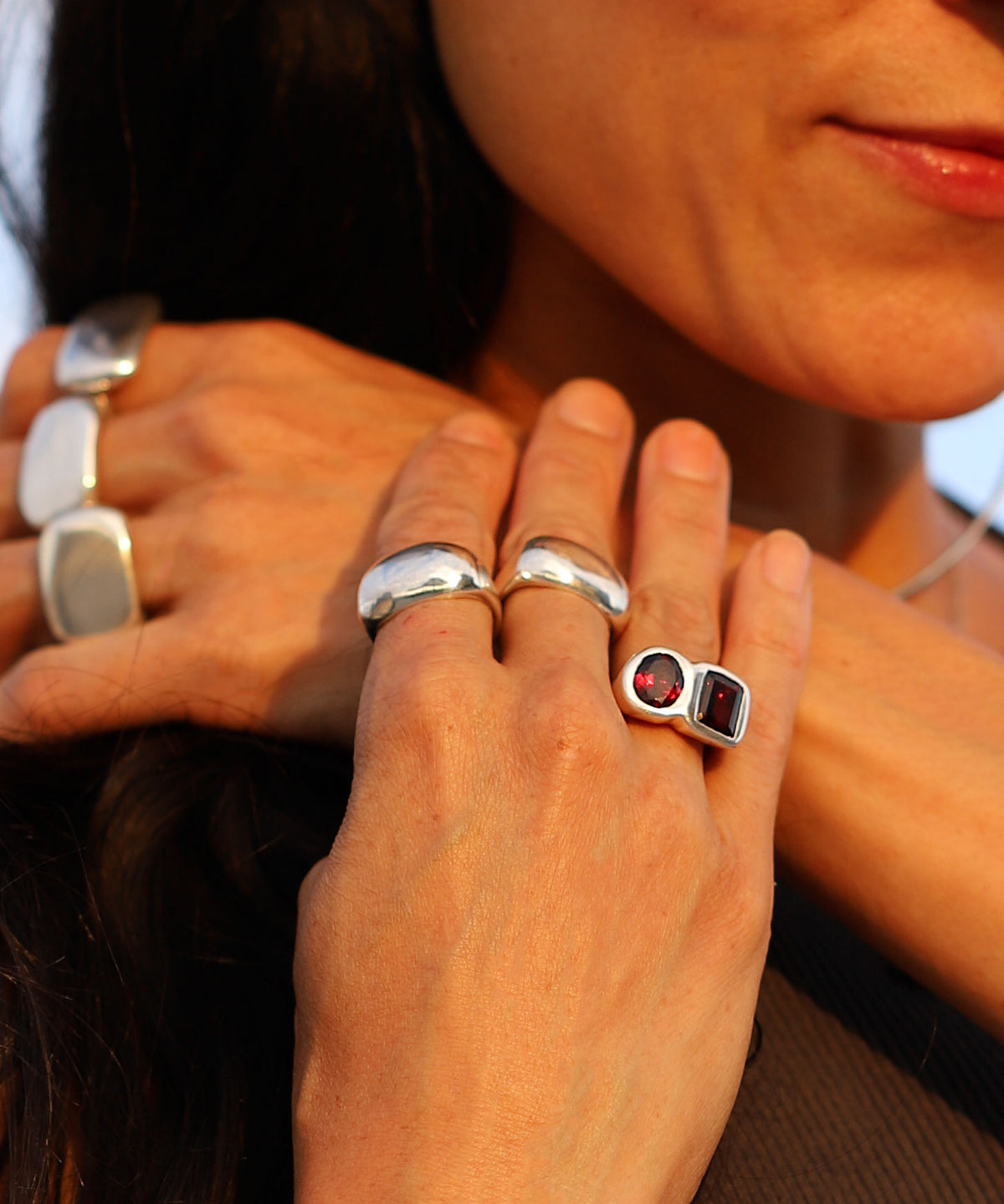 A close-up lifestyle shot of a person wearing multiple silver rings, including a prominent ring with a square-cut dark red gemstone.