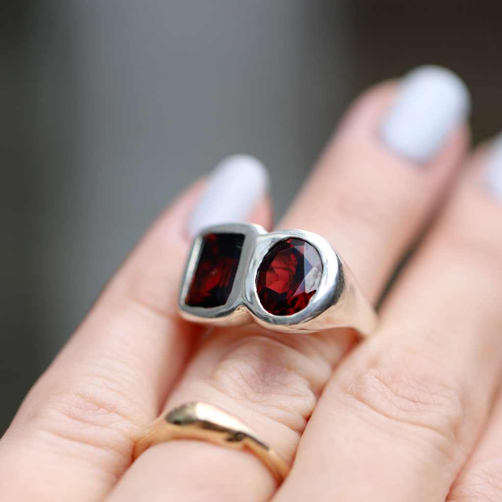 A close-up of a hand wearing a silver signet ring with two dark red gemstones, alongside a gold band ring.