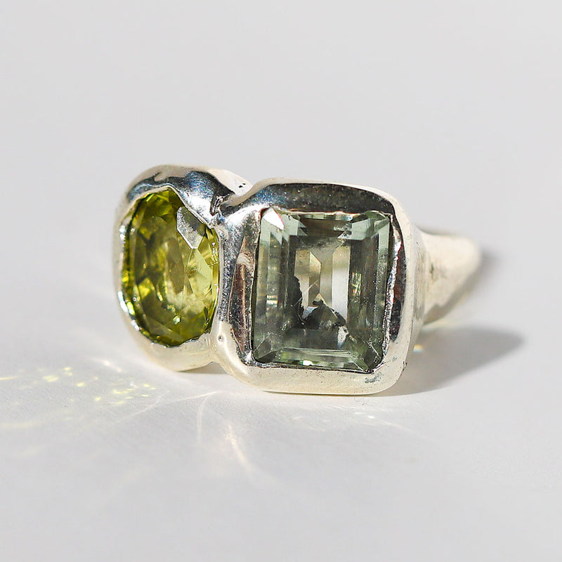 Silver ring with two green gemstones on a light gray background