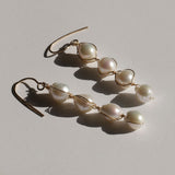 four white pearls wire wrapped earrings against off white background