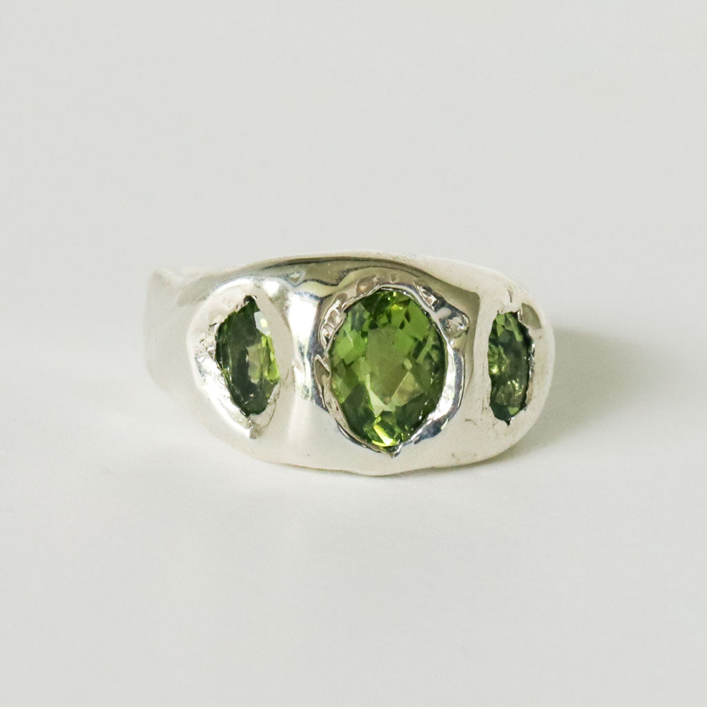 Silver ring with three green peridot gemstones on a white background