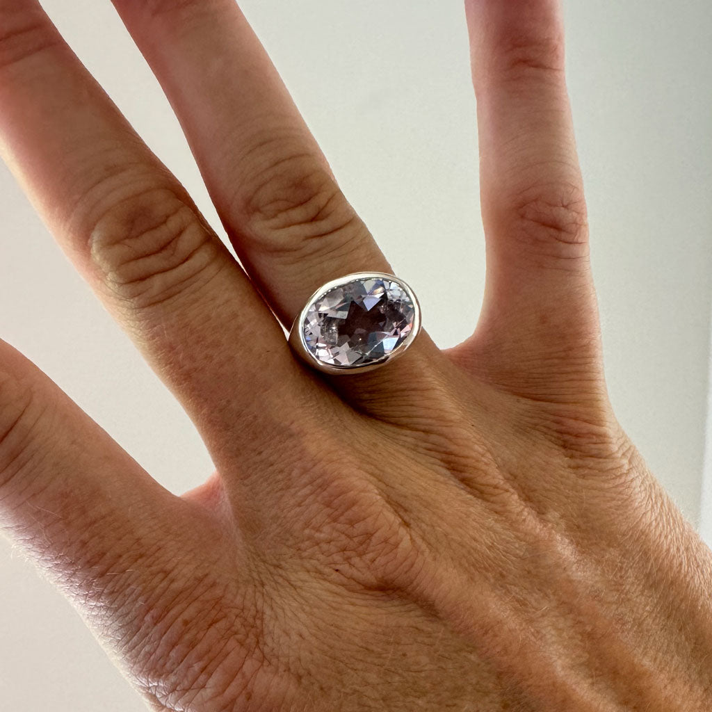 Hand wearing a ring with a large gemstone on a neutral background