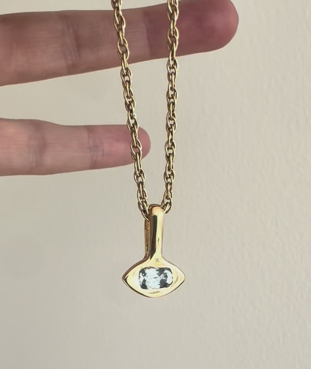 video of a gold eye-shaped pendant with blue montana sapphire on gold rope chain held by a hand
