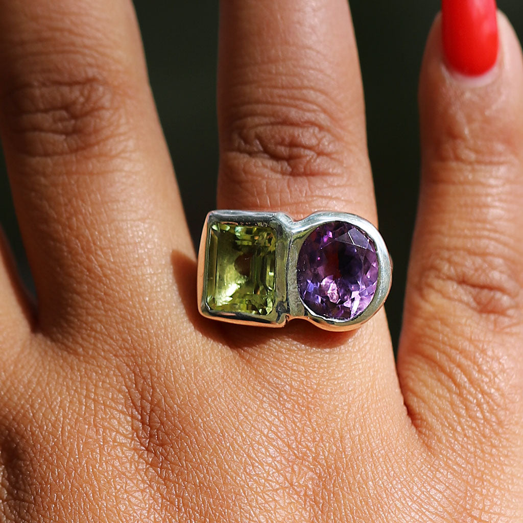 Close-up of a ring with green and purple gemstones on a person's finger.