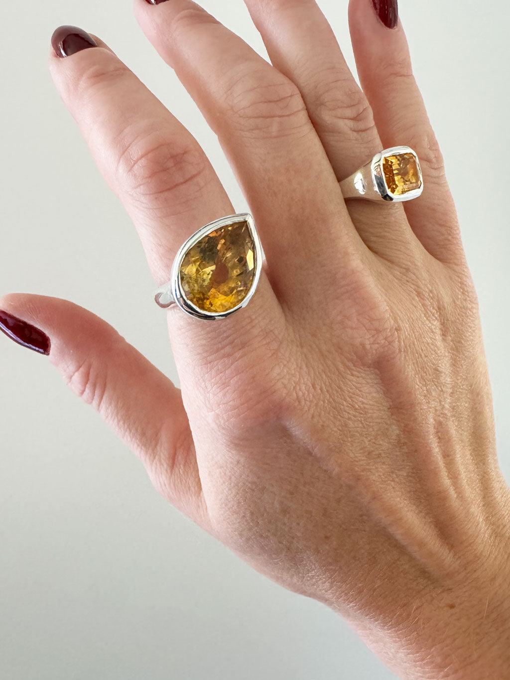 Hand wearing two silver rings with yellow gemstones on a light background