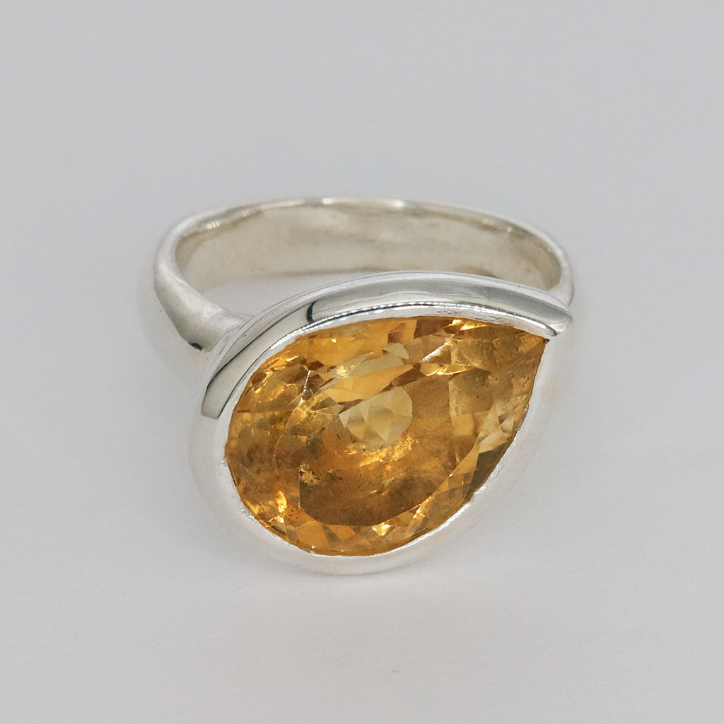 Silver ring with a large yellow citrine pear shaped gemstone on a light gray background