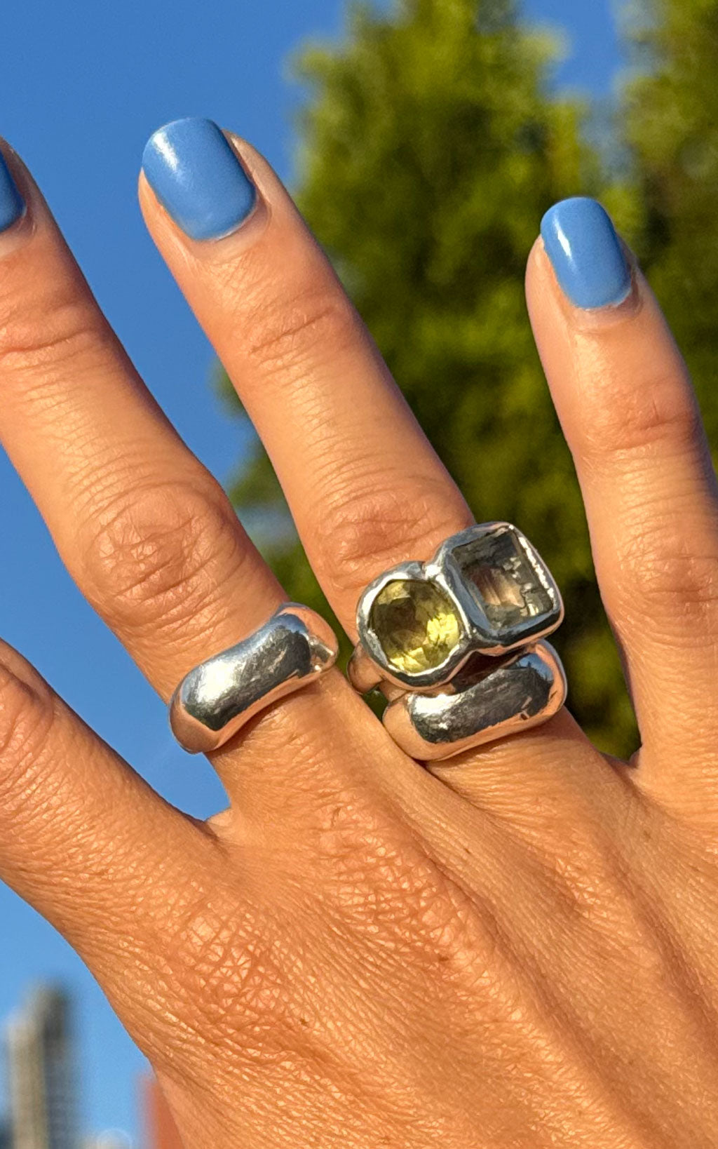 close up of hand with sky blue nails and chunky silver gemstone rings with lemon citrine and green amethyst
