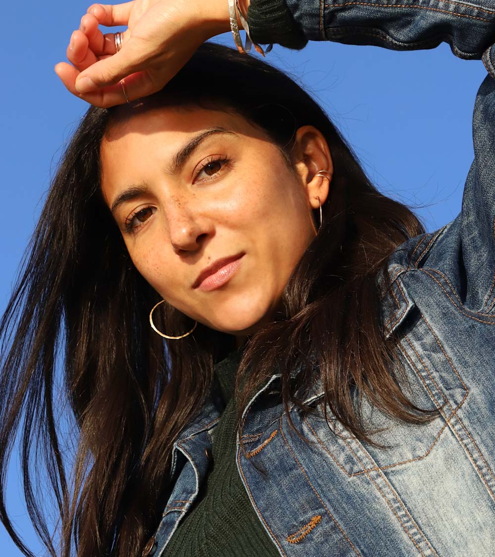 girl with small gold hoops jean jacket and blue sky