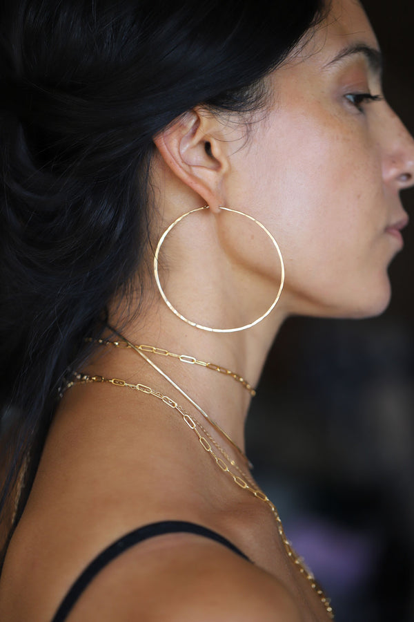 Brunette woman wearing layered gold necklaces and thin gold hoop earrings
