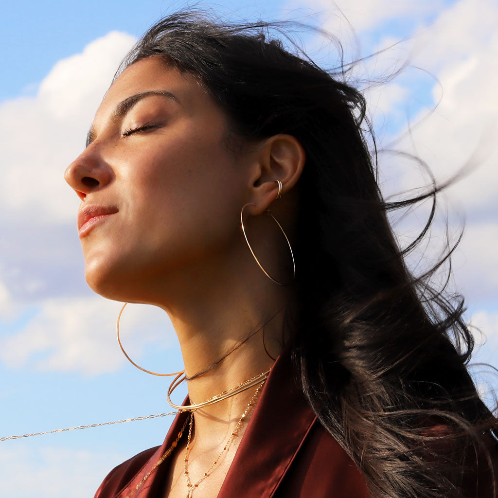 brunette on a red wine shirt against wind wearing two stacked 14k gold filled cartilage hoop earrings