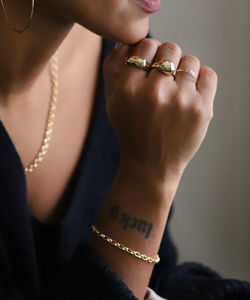 woman's hand with chunky gold rings and gold chain bracelet and lucky tattoo on wrist