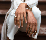 black woman hands close-up wearing globe ring thin gold stacking rings plateau ring and curved ring sitting on stairs