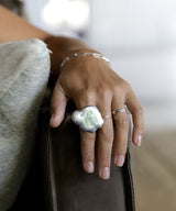 hand with extra large cloud shaped silver ring resting against leather couch arm