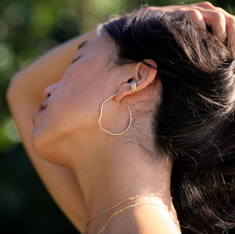 young woman wearing irregularly shaped gold hoop earrings and cartilage hoops