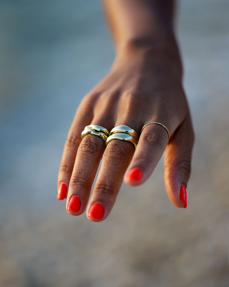 multiple chunky organically shaped gold rings on brown hand with bright red nails