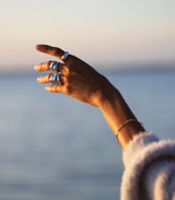 Woman's hand wearing six silver big rings and a silver link bracelet at the ocean  