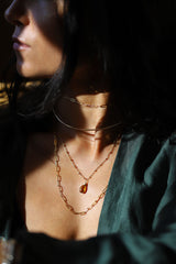Brunette woman wearing four layered gold necklaces, and green shirt