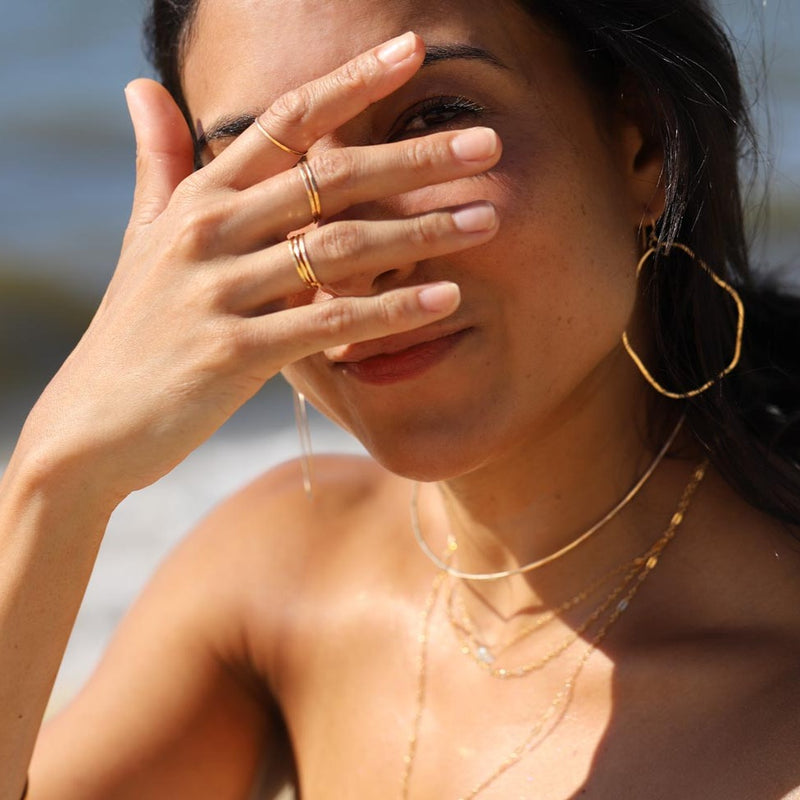 girl peering between fingers with thin gold stacking rings