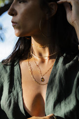 Brunette woman wearing four layered gold necklaces, Hoop earrings, and green shirt