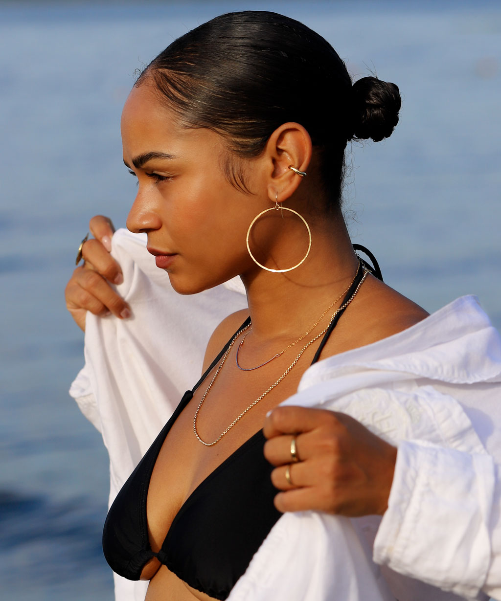 side view of girl in black bikini top and loose white open shirt wearing gold jewelry