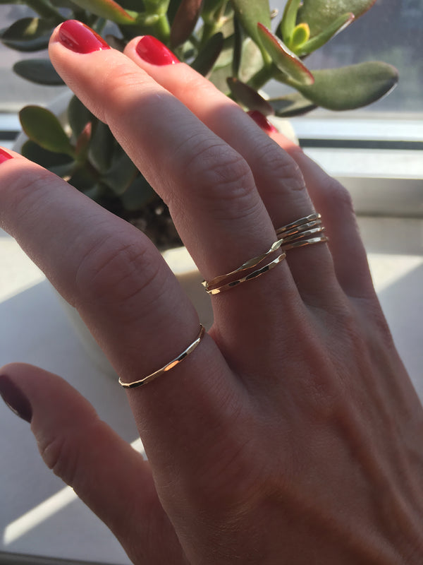 red nails hand wearing 14k gold filled wavy and flat rings on index middle and ring fingers with a green plant on background
