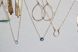 14k gold filled good luck horseshoe necklace on a grey surface next to other pieces of delia langan jewelry