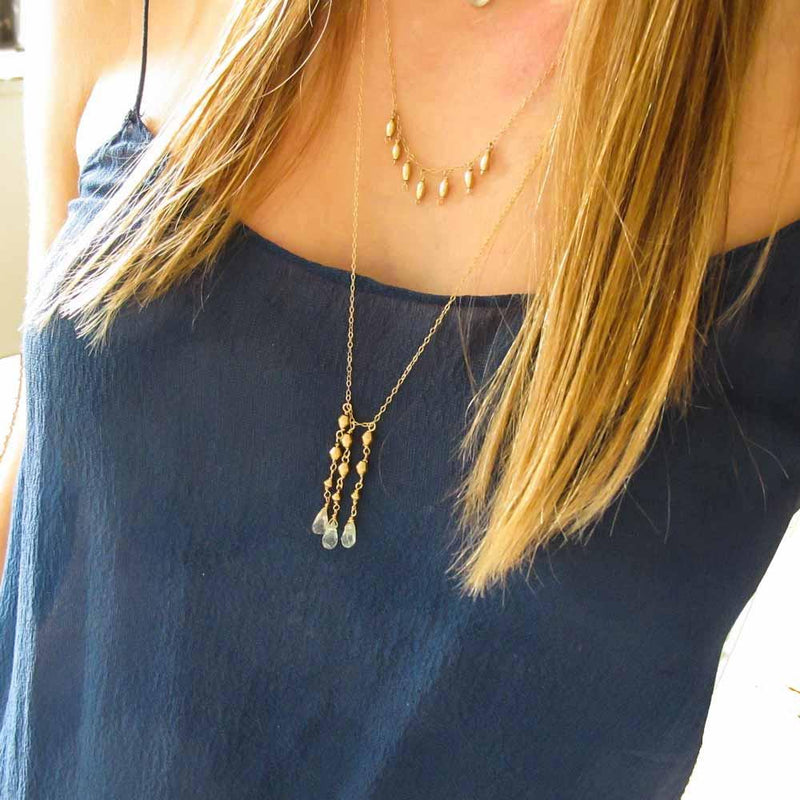 breast closeup of a blond woman with a navy blue top wearing a 14k gold filled aquamarine tassel multi gemstone necklace 