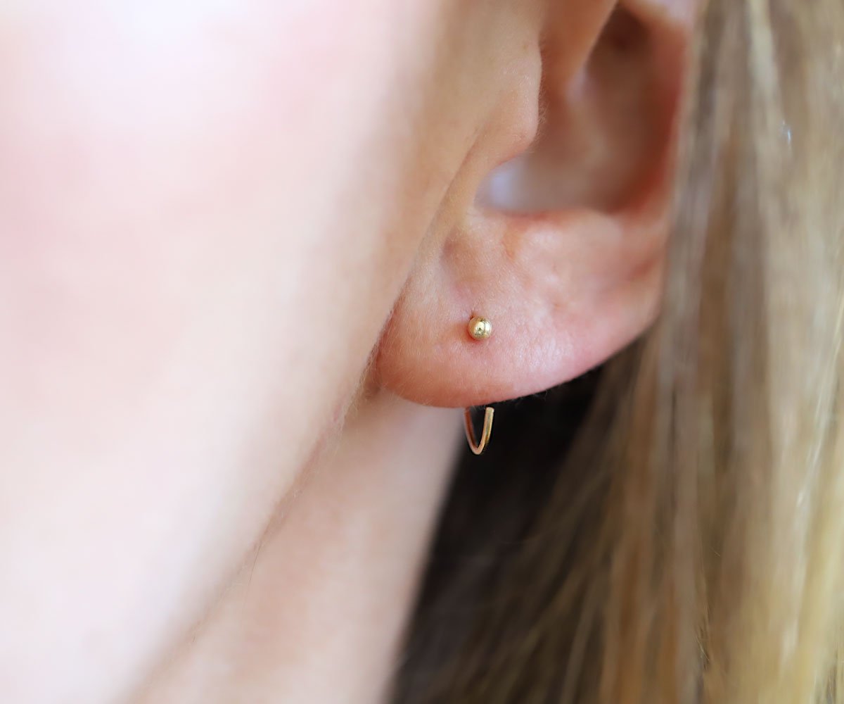tiny gold ball end hug hoops in an ear